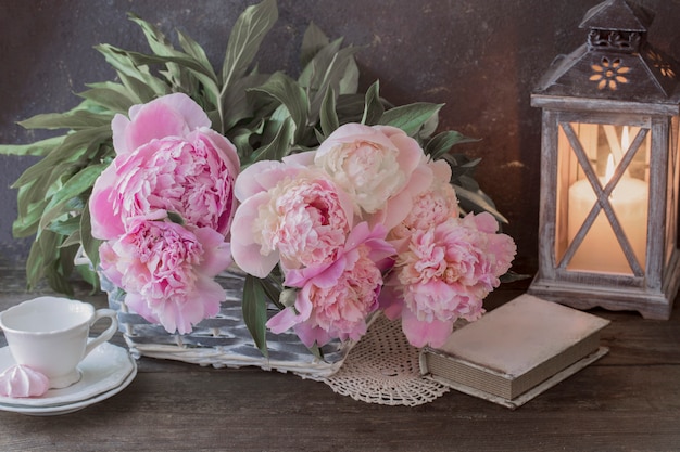 Photo un bouquet de pivoines roses, une bougie dans un chandelier en forme de lanterne, un livre, une tasse