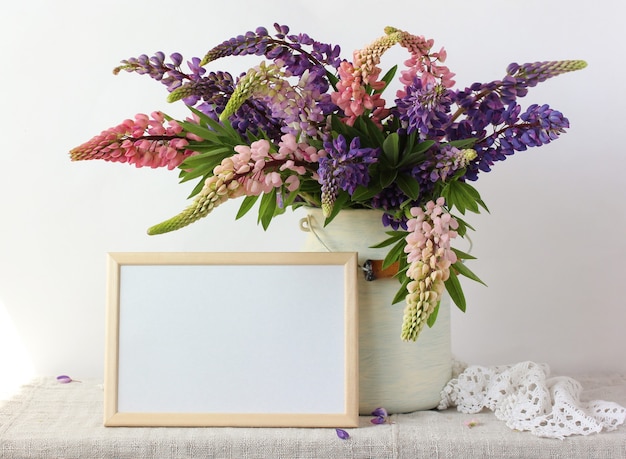 Bouquet de pivoines roses et violettes dans une boîte et un cadre rectangulaire vide sur la table.