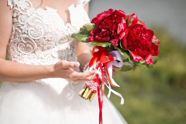 Un bouquet de pivoines rouges entre les mains d'une mariée en robe de mariée 2823