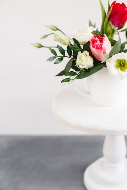 Bouquet de printemps dans un vase blanc sur un support blanc en bois. Roses, tulipes et lisianthus.