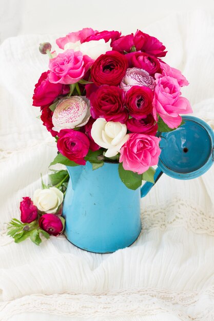 Bouquet de renoncules roses et fleurs roses en pot bleu sur blanc