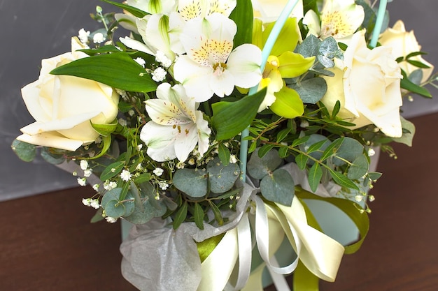 Bouquet de roses astralmeria et de lys dans un panier de couleur vert clair sur fond gris