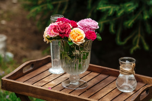 Bouquet de roses colorées dans un vase en verre sur une jambe sur un plateau en bois