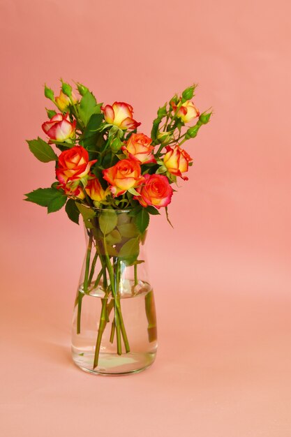 Un bouquet de roses dans un vase en verre sur fond rose.