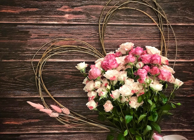 Un bouquet de roses roses avec un cadre en forme de coeur sur un fond en bois