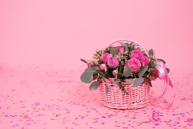 Bouquet de roses roses dans un panier en osier sur une table rose à l'arrière-plan anniversaire