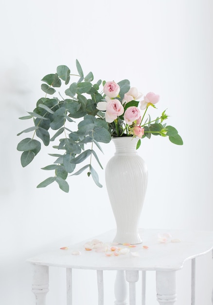 Bouquet de roses roses dans un vase blanc en céramique sur une étagère en bois vintage blanche