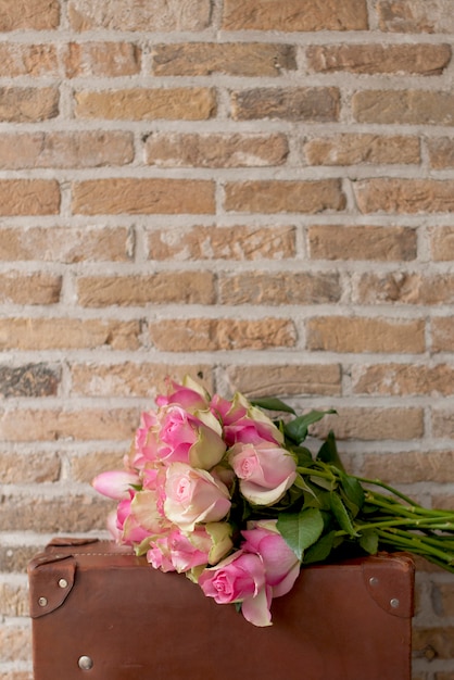 un bouquet de roses roses sur une valise brune près d'un mur de briques