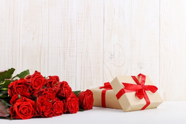 Un bouquet de roses rouges, un cadeau sur une table en bois blanche