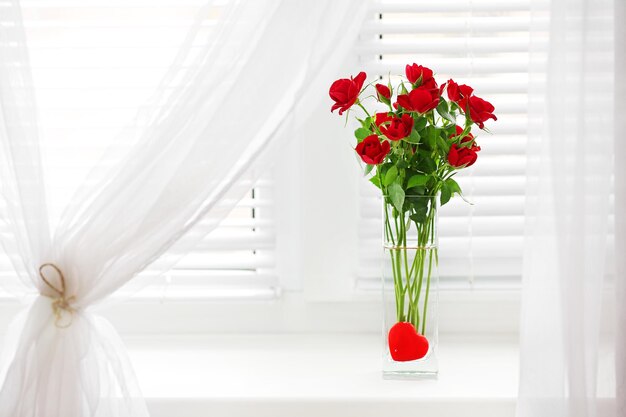 Bouquet de roses rouges dans un vase en verre avec coeur sur fond de rebord de fenêtre