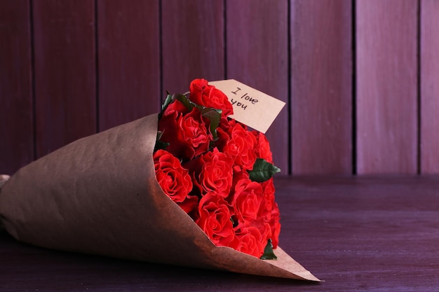 Bouquet de roses rouges avec étiquette enveloppée dans du papier sur fond de bois