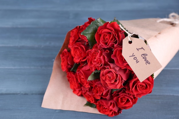 Bouquet de roses rouges avec étiquette enveloppée dans du papier sur fond de bois