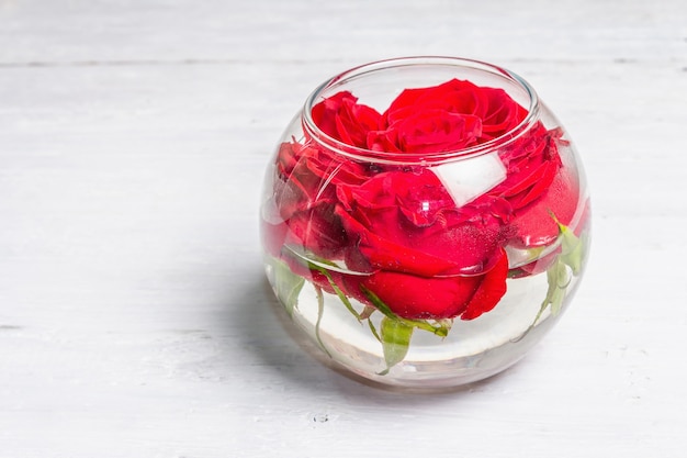 Bouquet de roses rouges fraîches dans un vase en verre. Le concept festif pour les mariages, les anniversaires, le 8 mars, la fête des mères ou la Saint-Valentin. Carte de voeux, planches de bois blanches