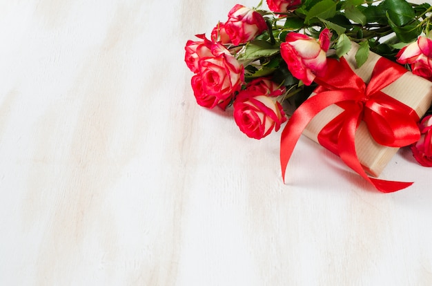 Bouquet de roses rouges et présent sur une table en bois.