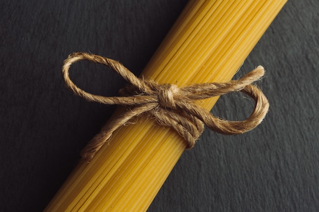 Bouquet de spaghettis crus allongé sur la surface en ardoise noire et attaché avec une corde