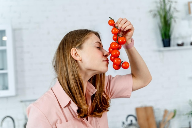 Bouquet de tomates cerises fraîches dans les mains de la femme sur fond de cuisine