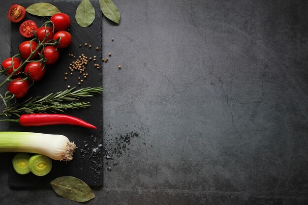 Bouquet de tomates cerises et racine de poireau avec des épices sur un fond noir Concept du menu Vue supérieure Espace de copie