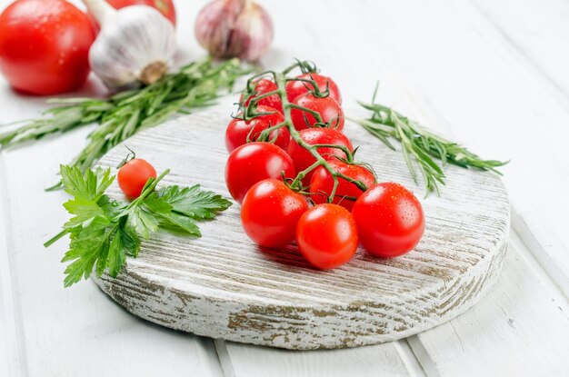 Bouquet de tomates cerises rouges avec de l'ail au romarin vert et des épices sur une vieille table blanche