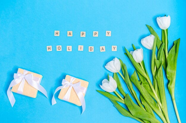 Bouquet de tulipes blanches avec des boîtes pour cadeaux et table bleue de joyeuses fêtes.