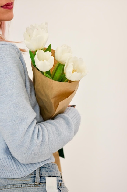 Bouquet de tulipes blanches dans une main féminine sur fond blanc.