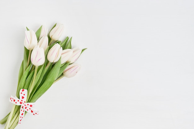 Bouquet de tulipes blanches décorées avec ruban coeurs sur fond en bois blanc