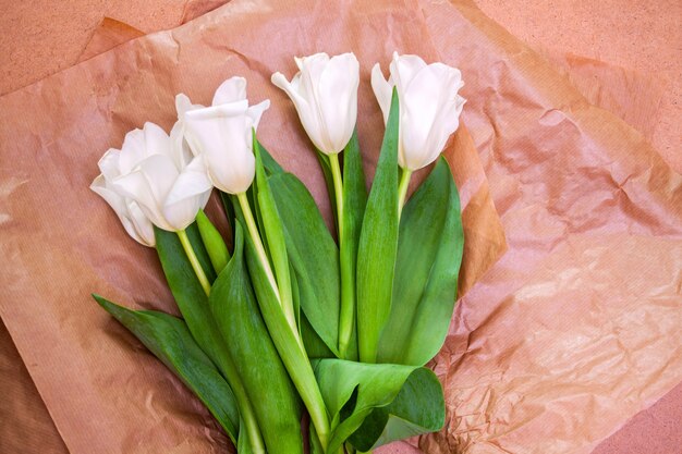 Bouquet de tulipes blanches délicates et lumineuses en papier kraft sur fond de plaque de bois