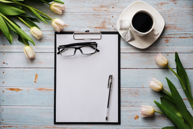 Bouquet de tulipes blanches avec un presse-papier vide et une tasse de café sur une table en bois