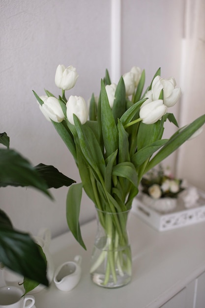 Un bouquet de tulipes blanches se dresse dans un vase sur un tableau blanc