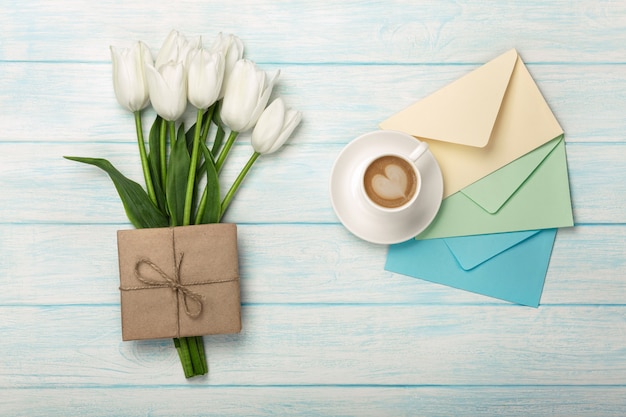 Un bouquet de tulipes blanches, une tasse de café avec une note d&#39;amour et des enveloppes de couleurs sur des planches en bois bleues. Fête des mères