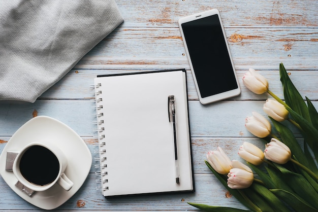 Bouquet de tulipes avec un cahier vide, une tasse de café et un téléphone sur un fond en bois