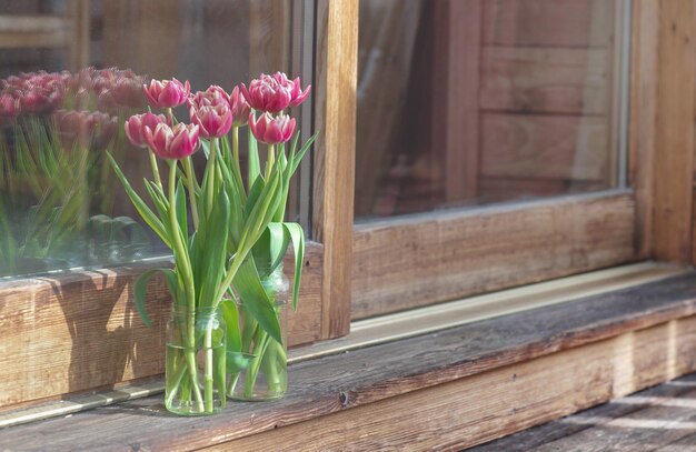 bouquet de tulipes dans un vase devant une fenêtre de baie sur une terrasse en bois