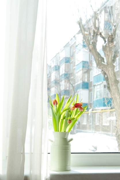 Un bouquet de tulipes dans un vase en fer sur le rebord de la fenêtre sur fond de ville enneigée