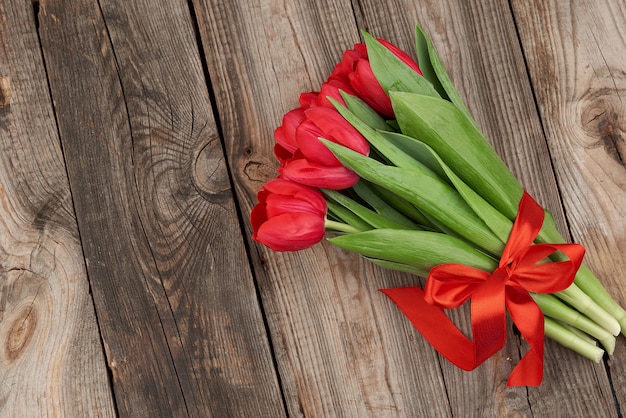 Bouquet de tulipes en fleurs rouges avec des tiges et des feuilles vertes attachées avec un ruban de soie rouge