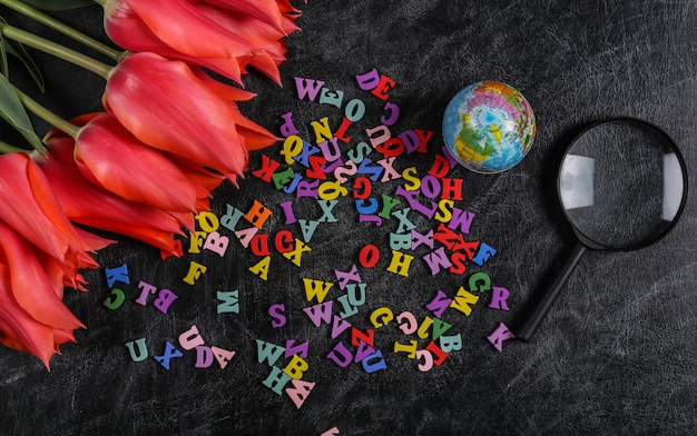 Bouquet de tulipes et fournitures scolaires, lettres sur tableau noir. Journée du savoir, retour à l'école. Vue de dessus