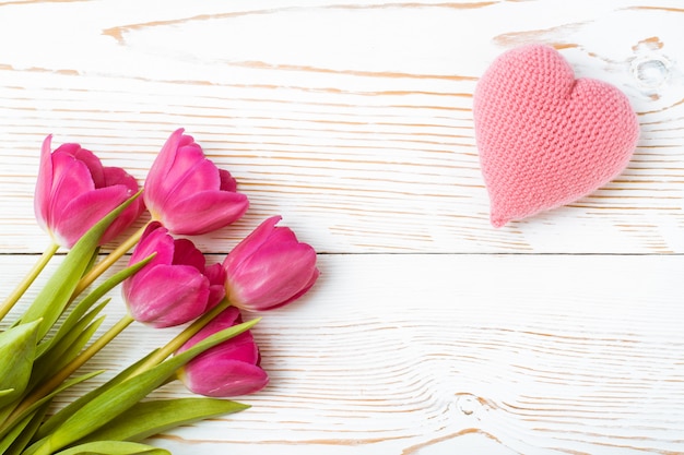 Un bouquet de tulipes fraîches et un coeur tricoté rose sur un bois blanc, vue de dessus