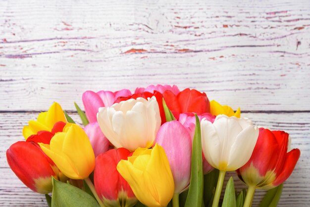 Un bouquet de tulipes fraîches, lumineuses et multicolores sur des planches en bois blanc.