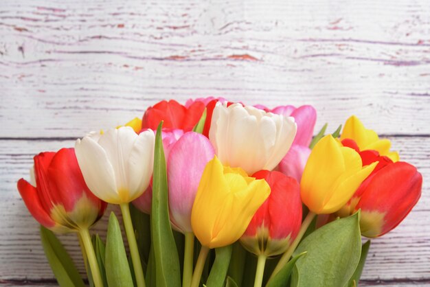 Un bouquet de tulipes fraîches, lumineuses et multicolores sur des planches en bois blanc.