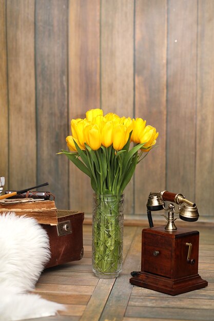 Un bouquet de tulipes jaunes dans un vase à l'intérieur d'une pièce rétro. Intérieur rétro avec bouquet de tulipes vieux téléphone et valise.