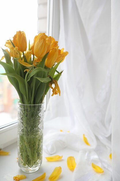 Un bouquet de tulipes jaunes dans un vase sur le rebord de la fenêtre. Un cadeau pour la journée d'une femme de fleurs de tulipes jaunes. Belles fleurs jaunes dans un vase près de la fenêtre.