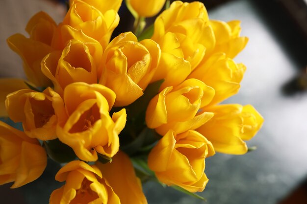 Un bouquet de tulipes jaunes fraîches dans un vase sur une table près de la fenêtre