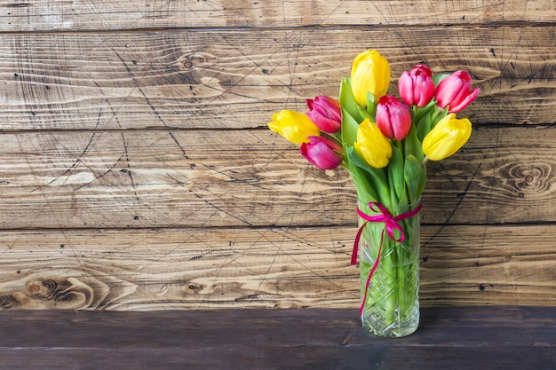 Bouquet de tulipes jaunes et roses sur un fond en bois.