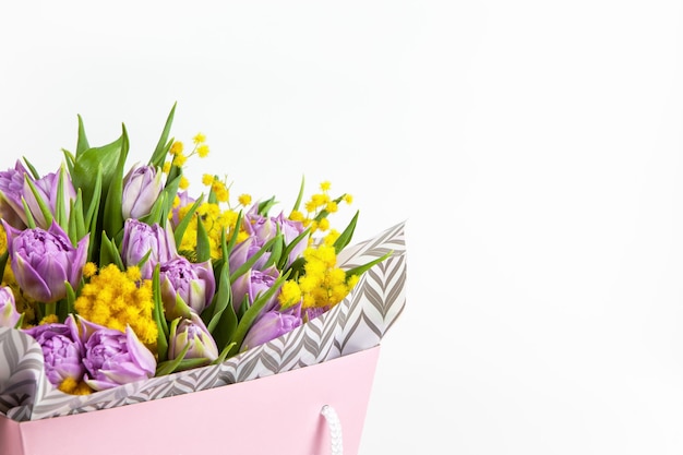 Bouquet de tulipes lilas et mimosas jaunes en boîte rose sur blanc