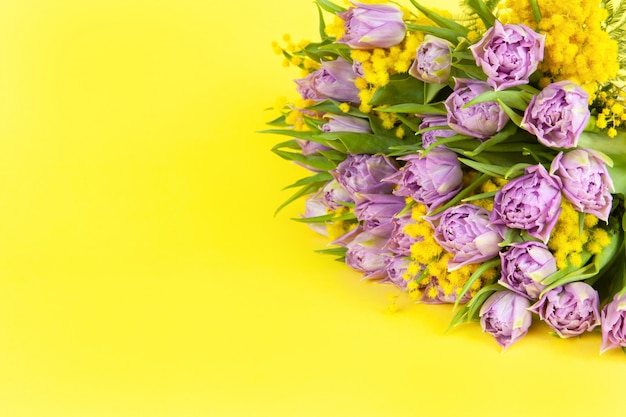 Bouquet de tulipes lilas et mimosas jaunes sur fond jaune, copie espace, vue latérale, gros plan.