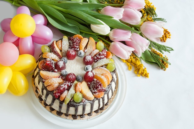 Bouquet de tulipes et mimosa, ballons comme fleurs et grand gâteau à la crème aux fruits