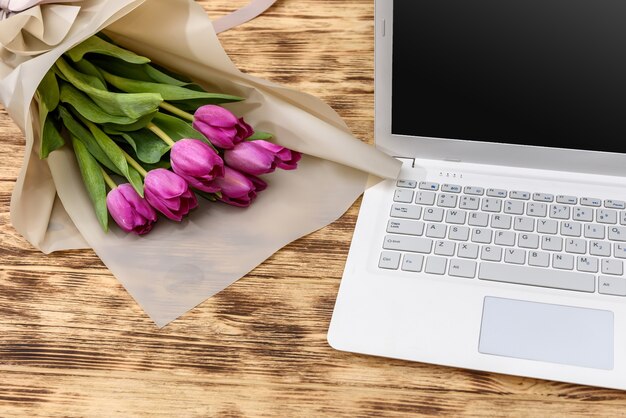 Bouquet de tulipes et ordinateur portable sur table en bois