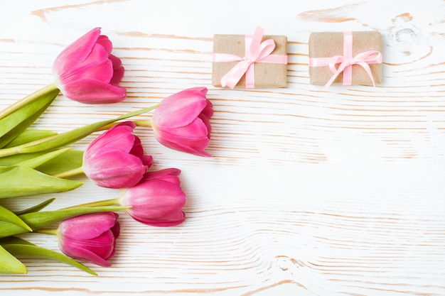 Bouquet de tulipes roses et cadeaux emballés sur un bois blanc, vue de dessus