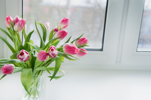 Photo un bouquet de tulipes roses dans un bocal en verre se trouve sur le rebord de la fenêtre de la maison.