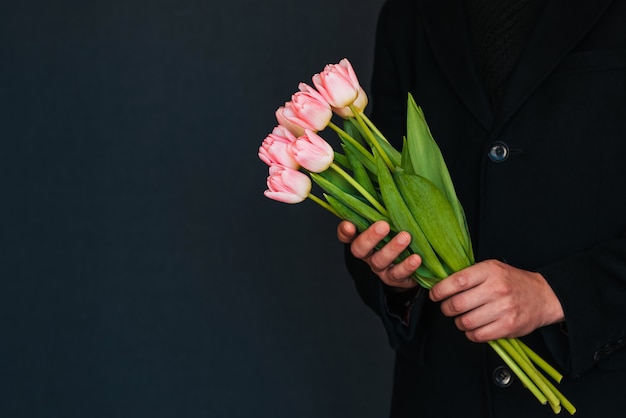 Bouquet de tulipes roses dans les mains d'un homme en habit noir