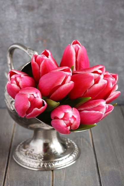 Bouquet de tulipes roses dans un vase en métal sur fond en bois