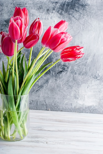 Bouquet de tulipes roses dans un vase en verre sur fond gris.